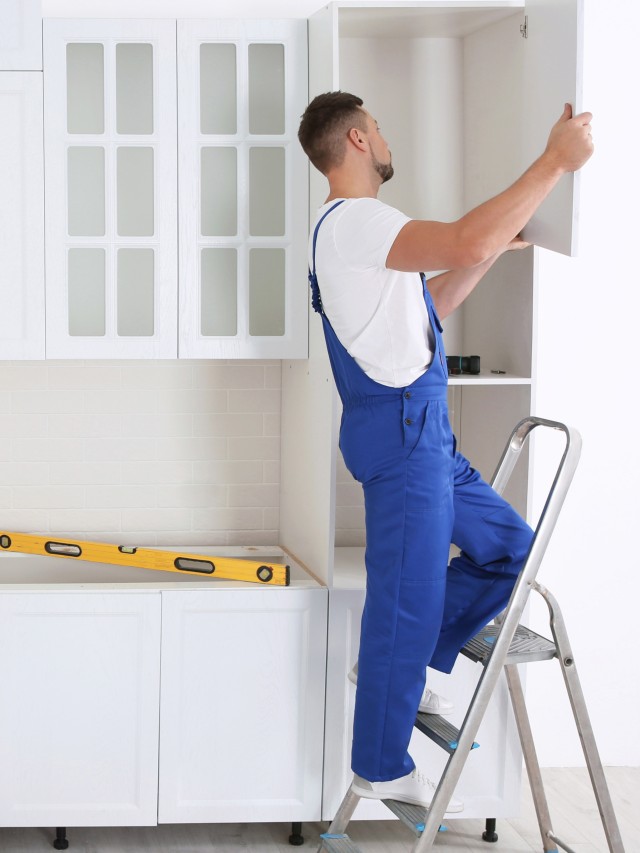 Worker installing door of cabinet in kitchen